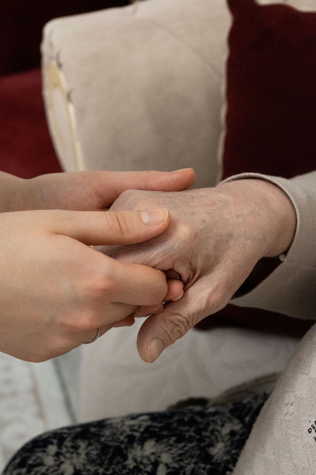 Close-up of a younger person's hands holding an older person's hand indoors
